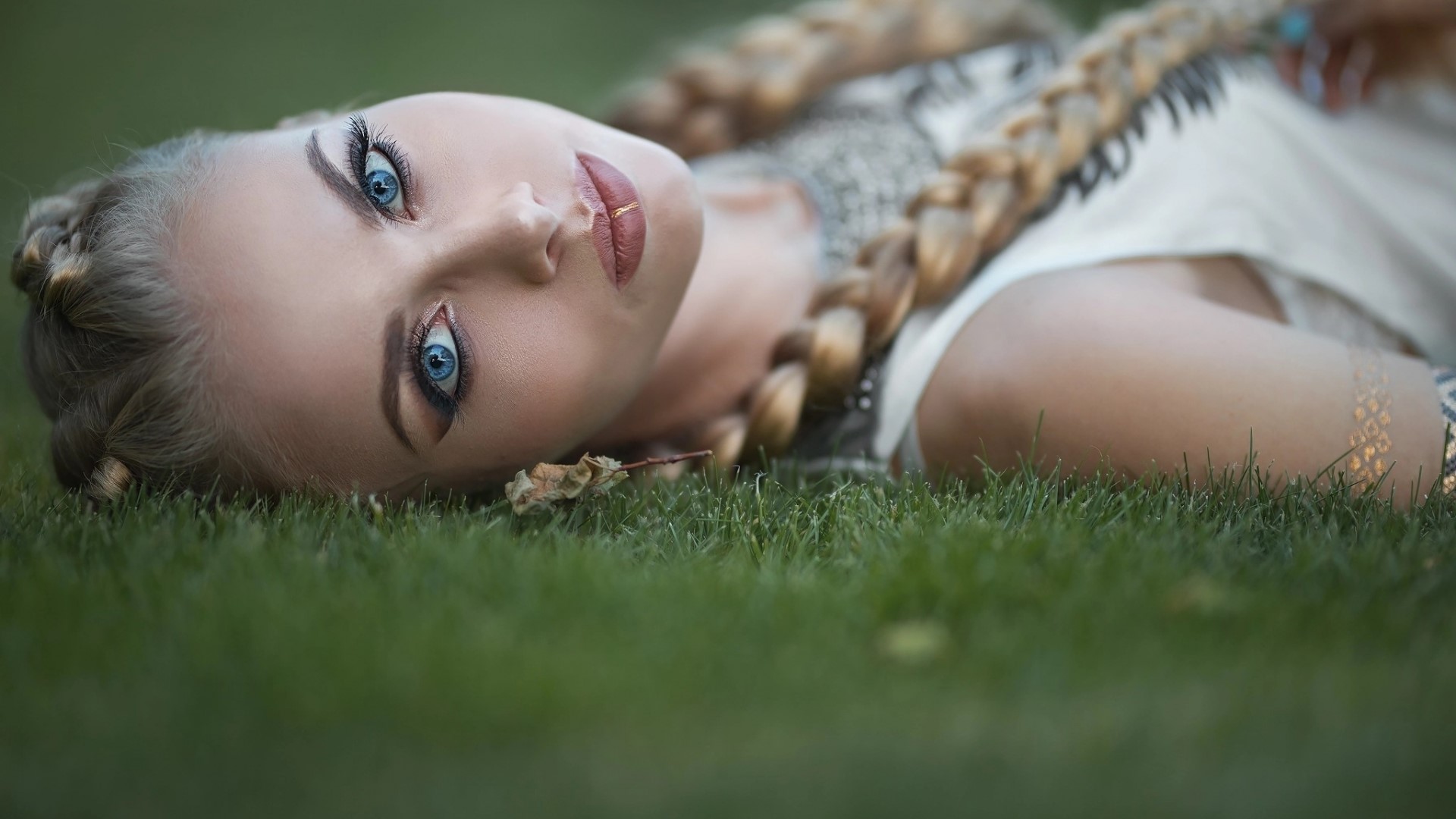 Woman with blue eyes and braids lying on grass HD Wallpaper