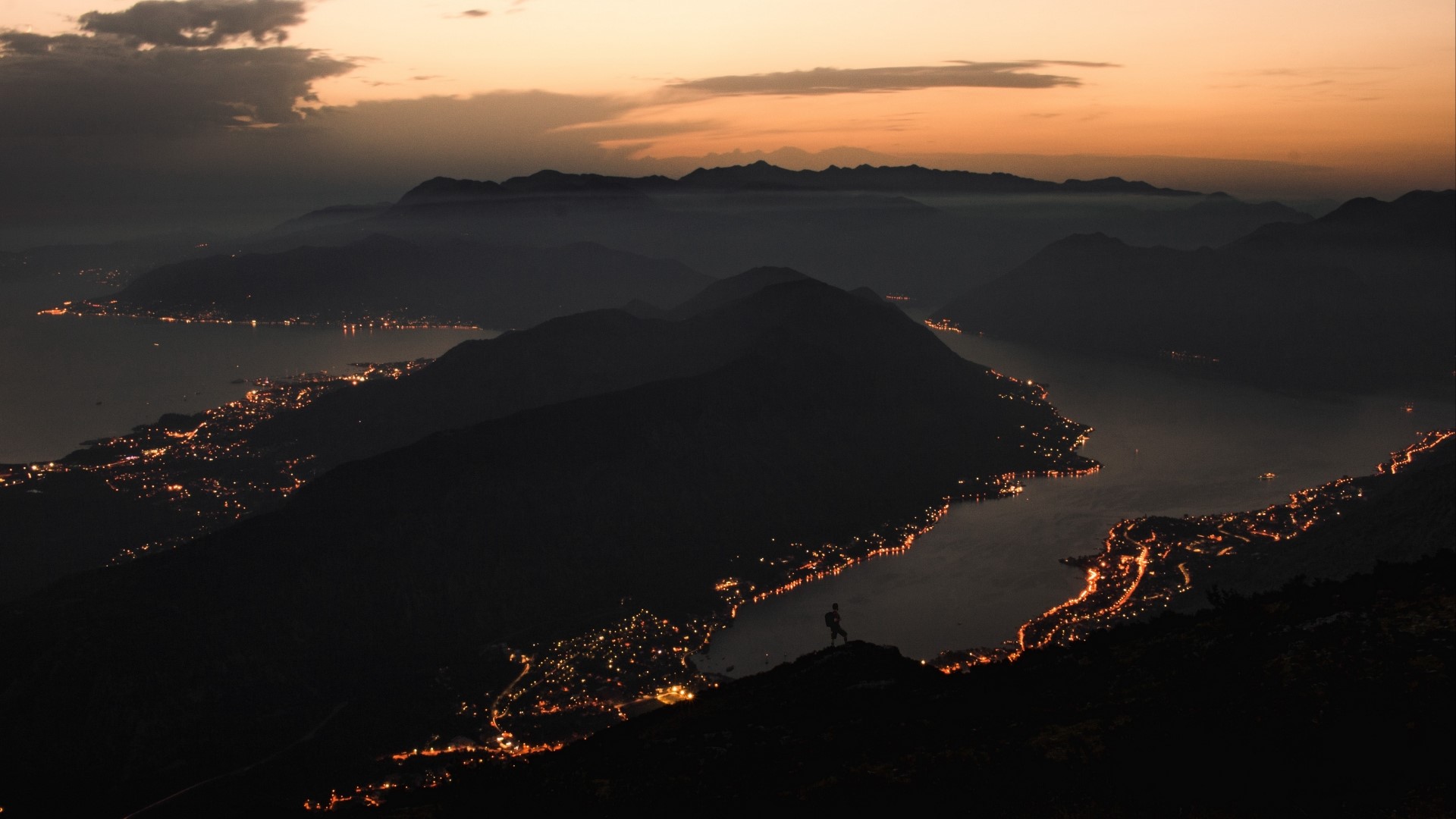 Silhouette of a person on a mountain overlooking a lake at sunset HD Wallpaper