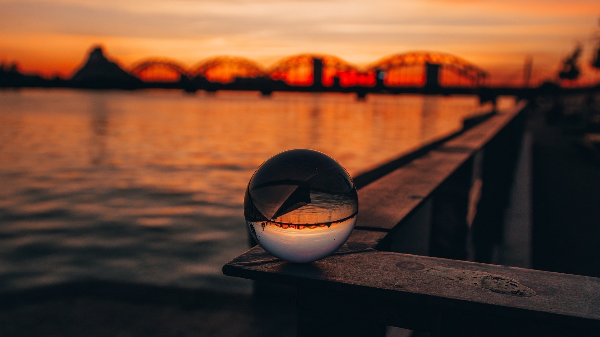 Crystal ball reflecting sunset over water with bridges HD Wallpaper