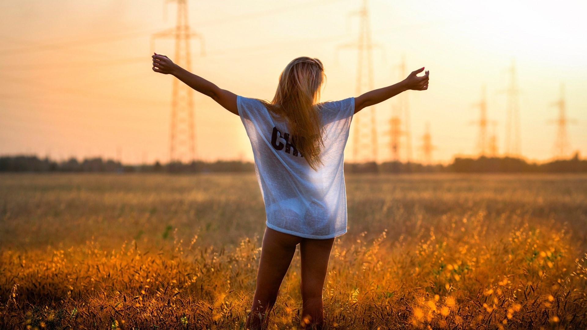 Woman with arms outstretched in a field at sunset HD Wallpaper