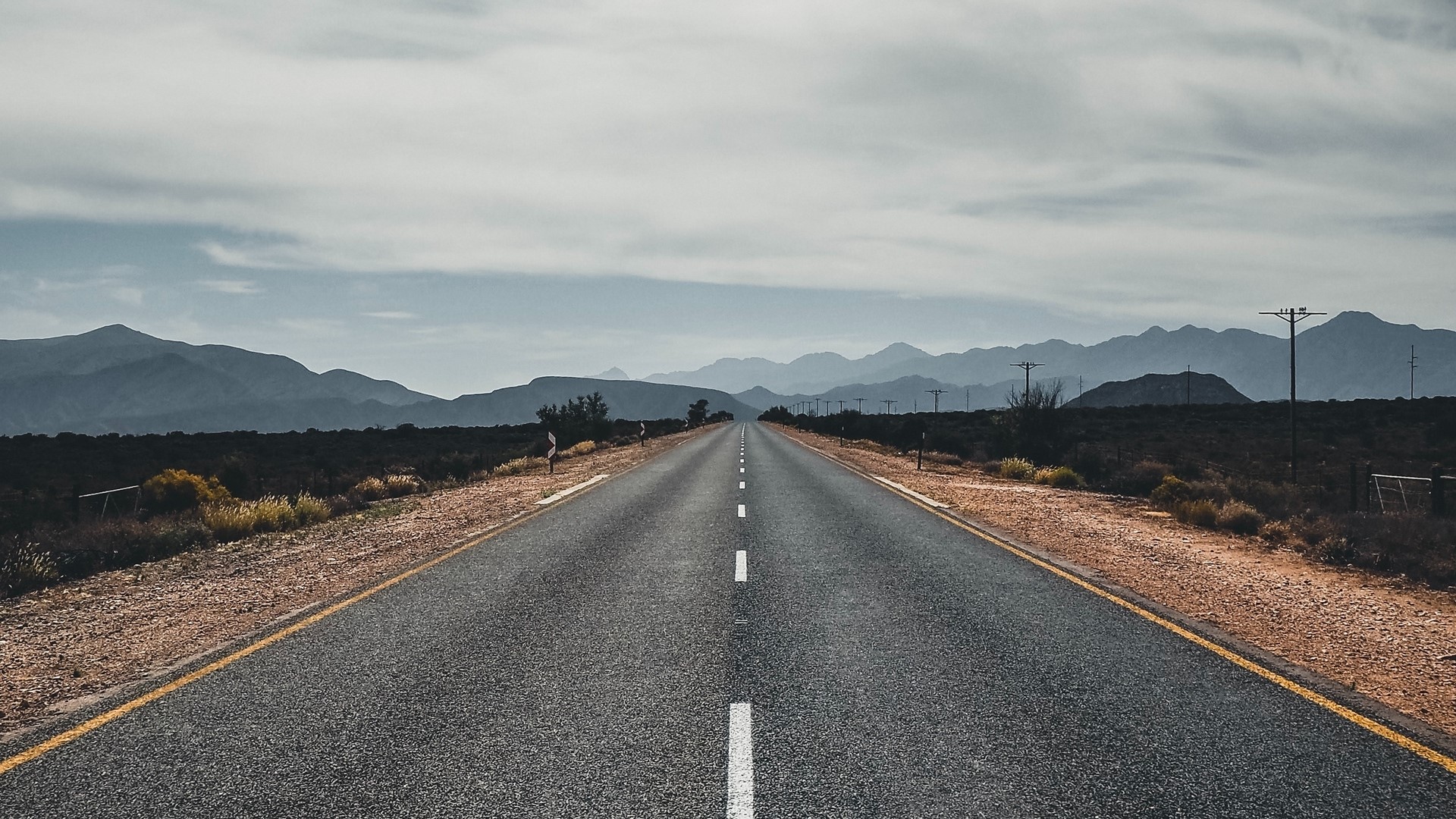 Empty highway stretching towards distant mountains HD Wallpaper