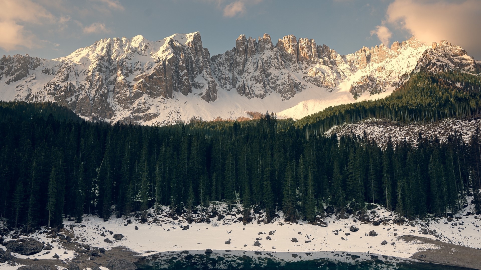 Snow-capped mountains above a pine forest and lake HD Wallpaper
