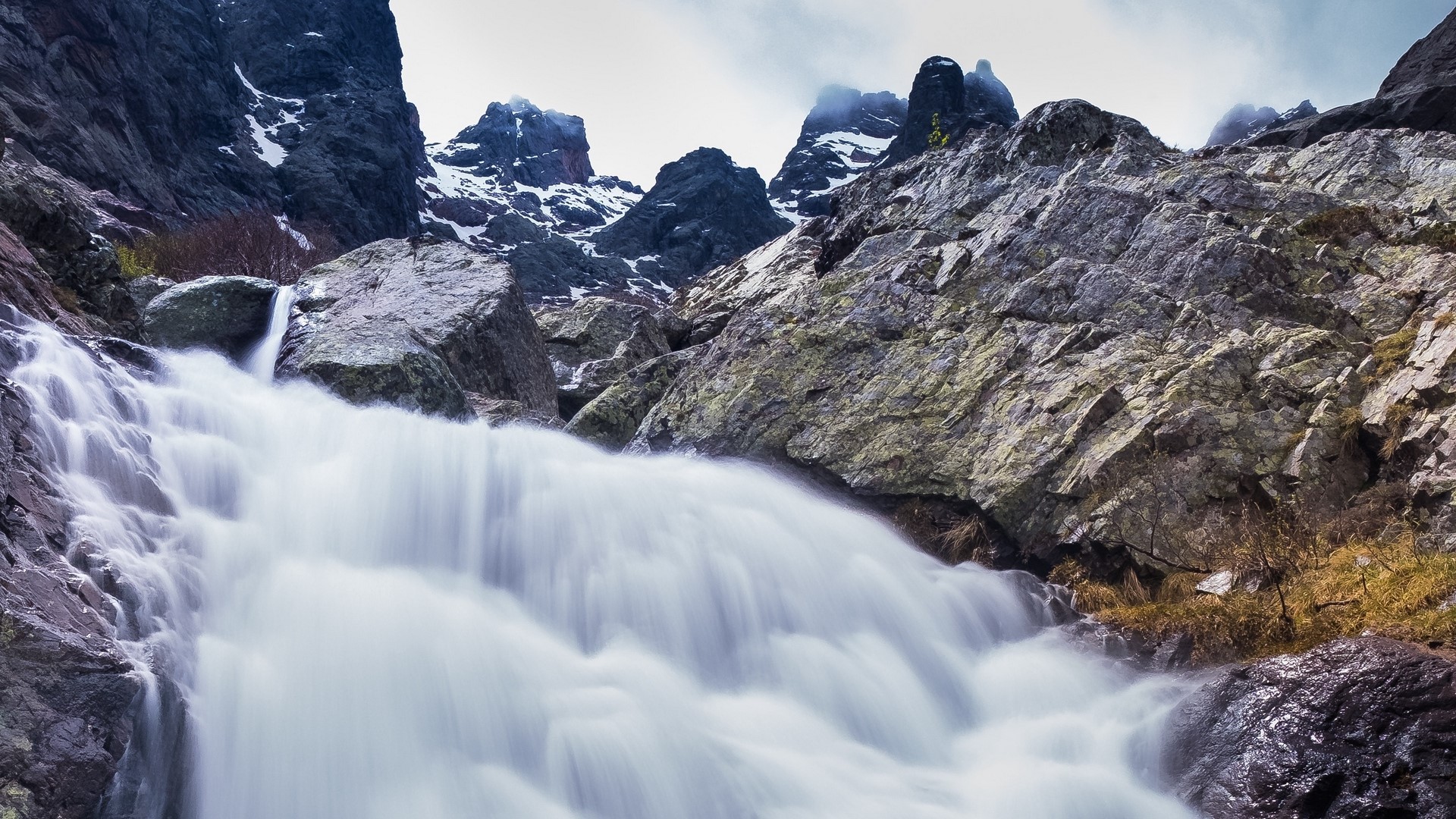 Waterfall cascading down rocky mountain HD Wallpaper