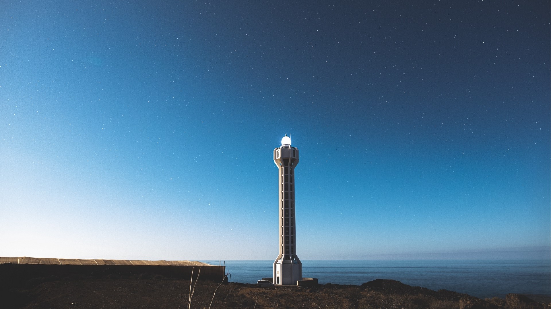 Lighthouse under a starry night sky HD Wallpaper
