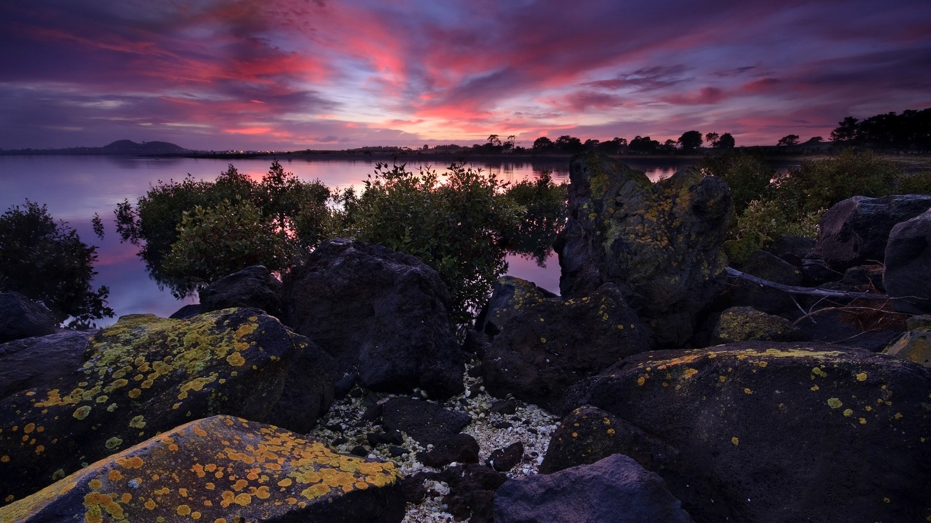 Sunset over a calm lake with rocky shore HD Wallpaper