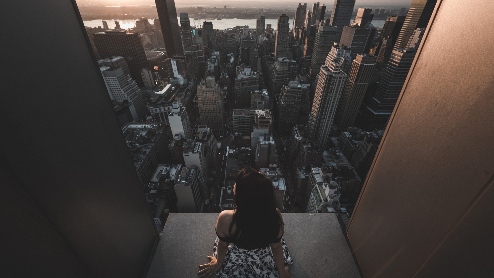 Woman sitting on edge of skyscraper overlooking New York City HD Wallpaper