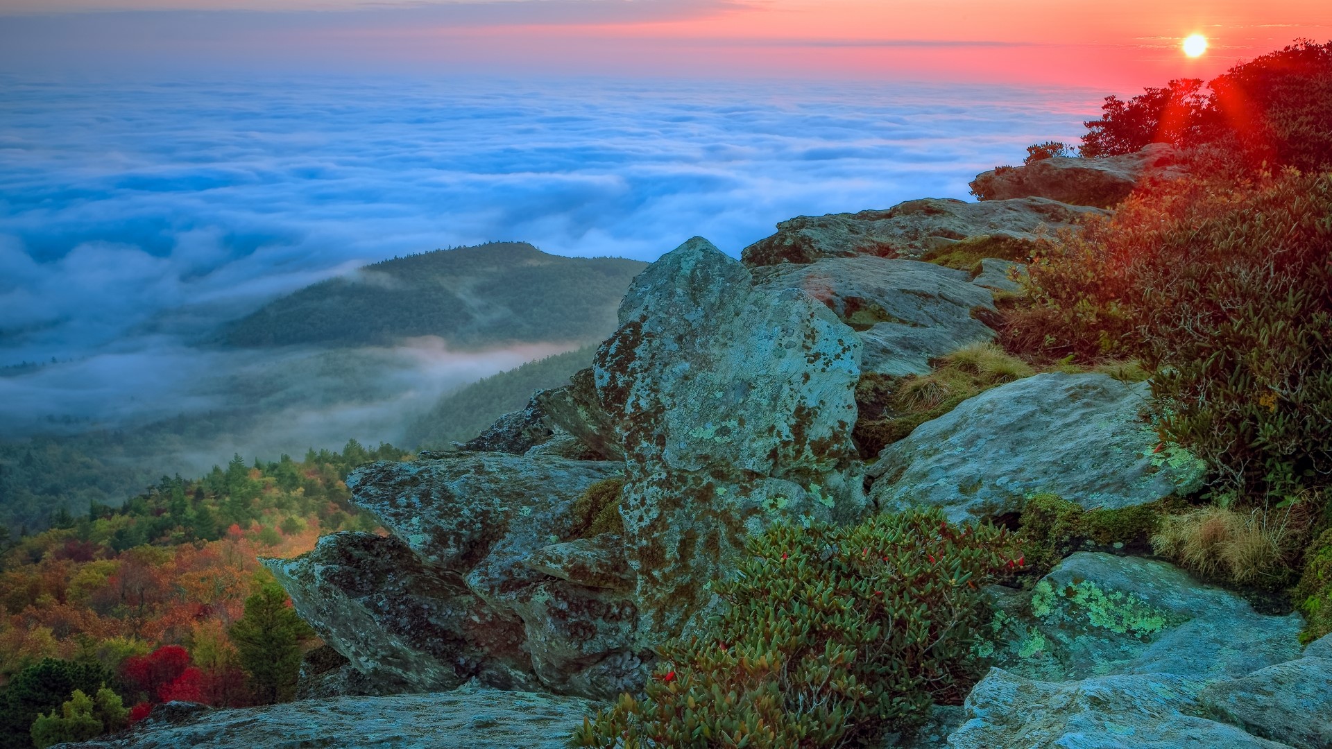 Sunrise over a foggy mountain valley with rocky foreground HD Wallpaper