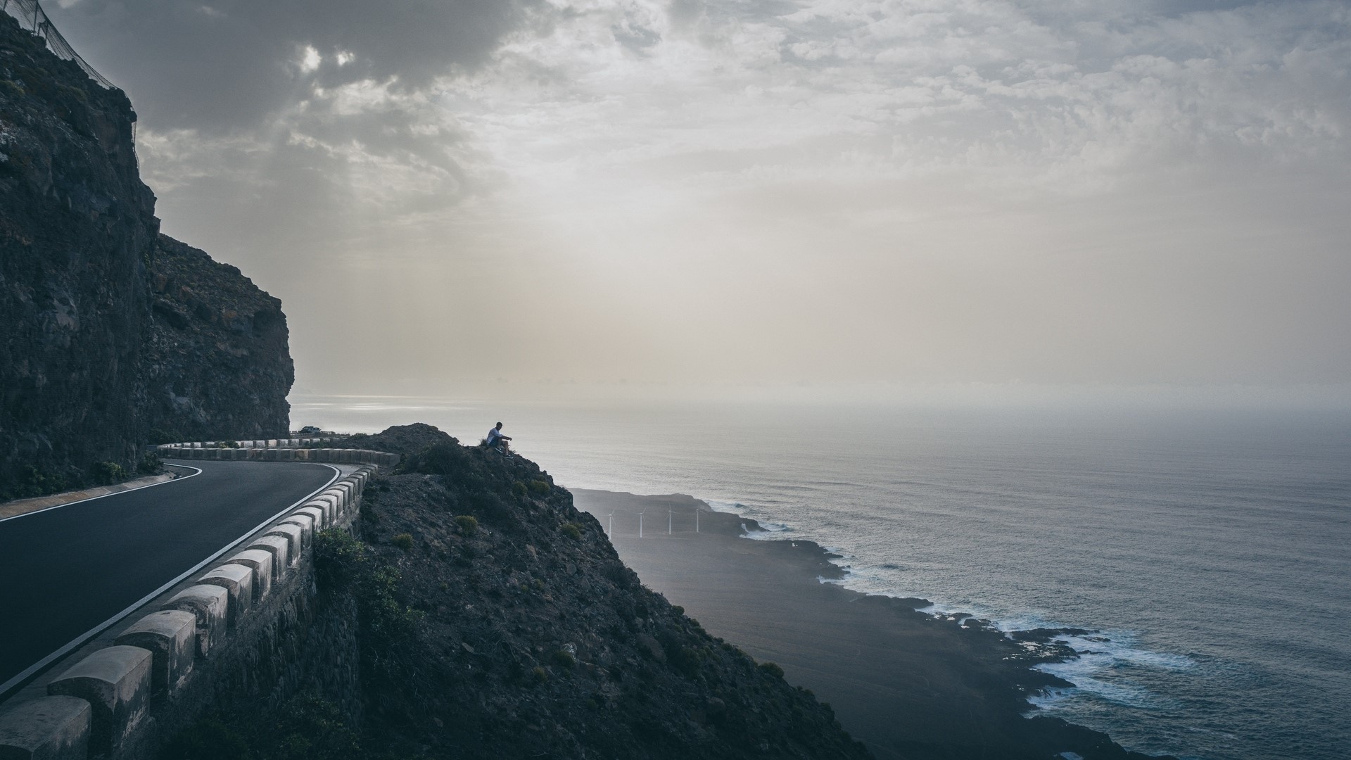 Person sitting on a cliff overlooking the ocean HD Wallpaper