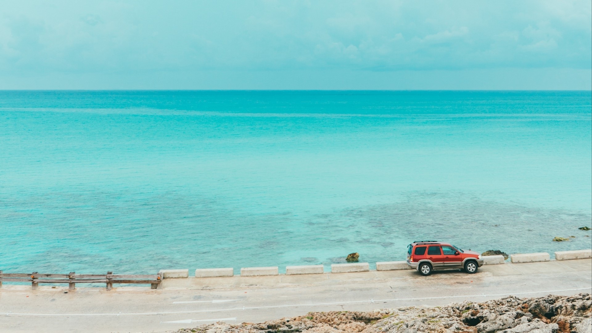 Red SUV parked by turquoise ocean on a sunny day HD Wallpaper