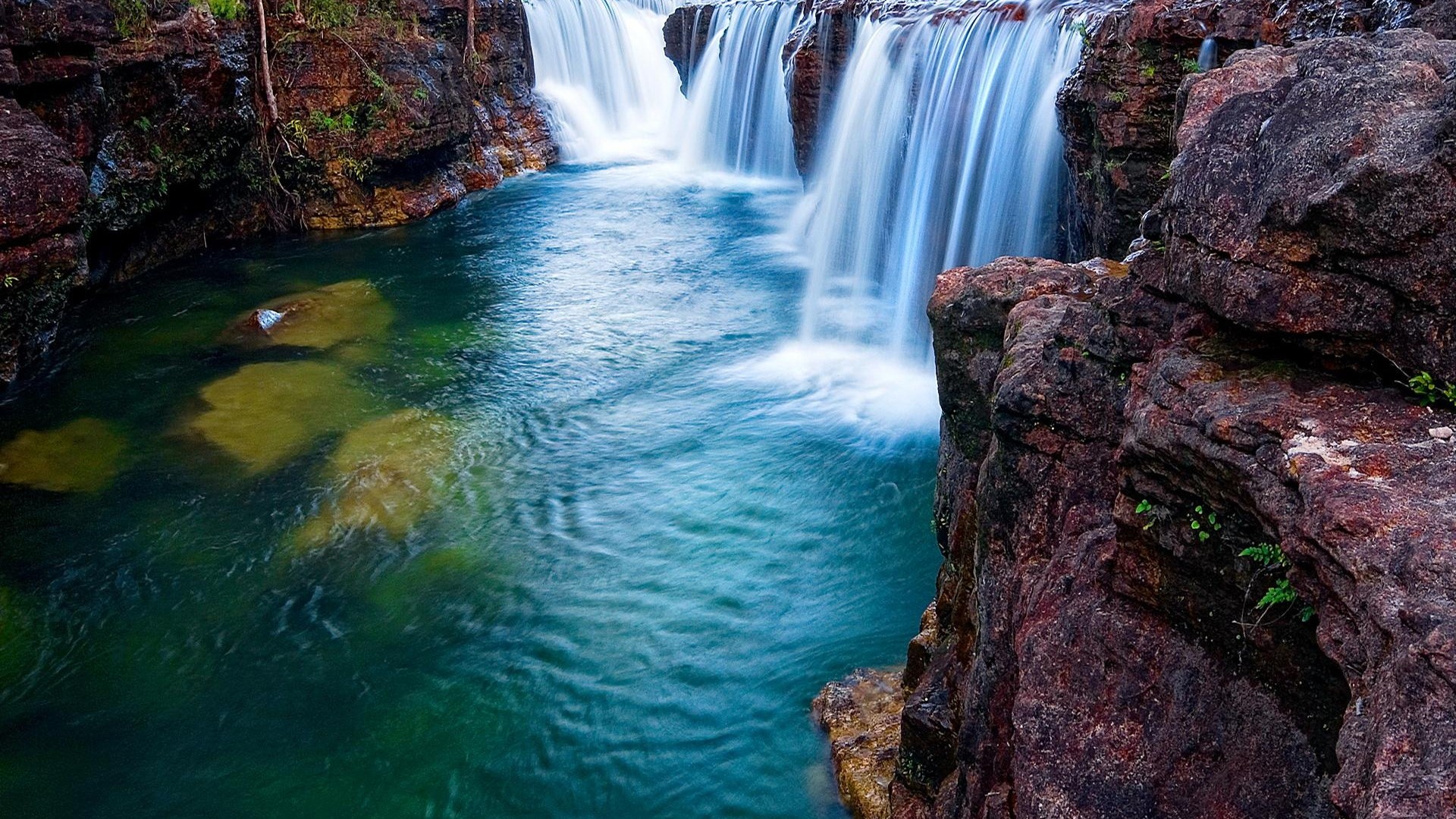 Waterfall cascading over rocks into a pool HD Wallpaper