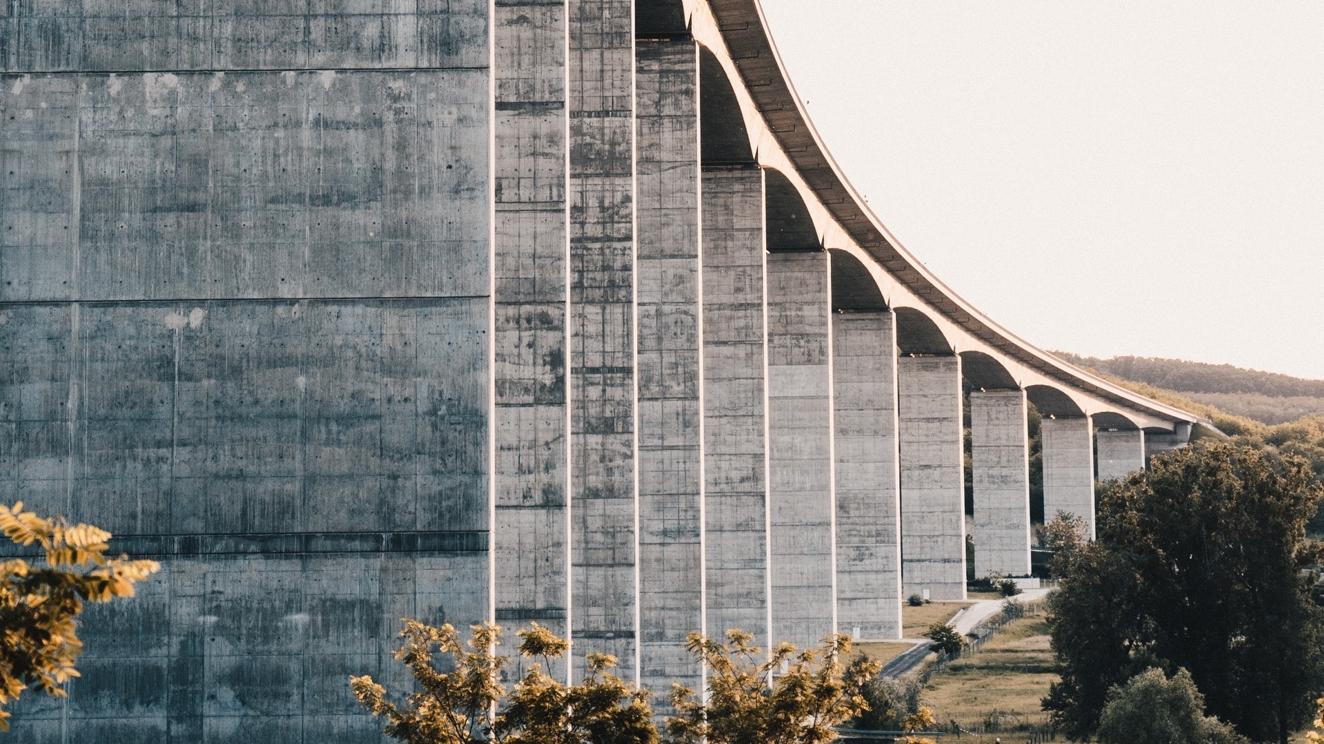 Concrete bridge with arched supports over a landscape HD Wallpaper
