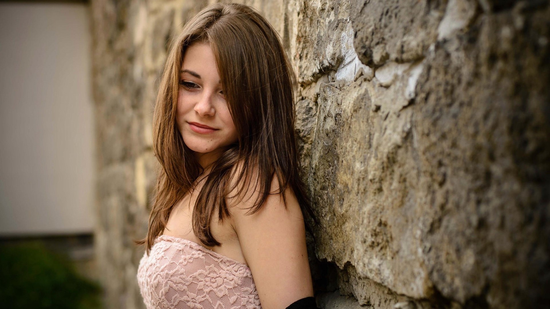 Girl leaning against a stone wall HD Wallpaper