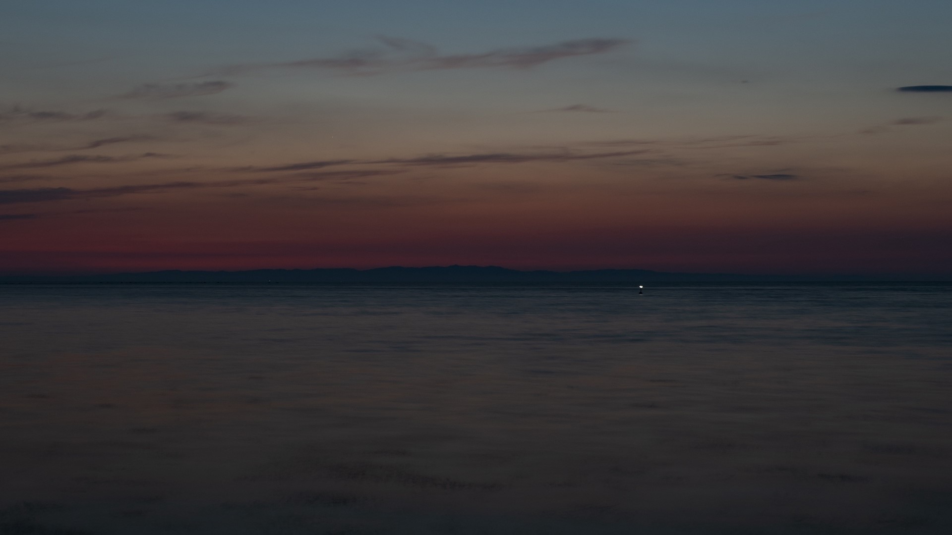 Sunset over the ocean with distant mountains HD Wallpaper