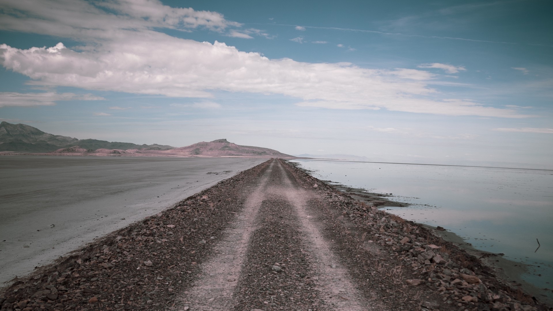 Dirt road along a salt flat and body of water HD Wallpaper
