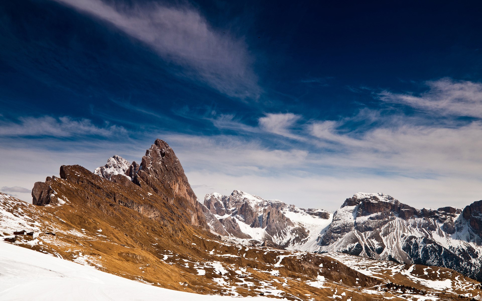 Snow-dusted mountains under a cloudy blue sky HD Wallpaper