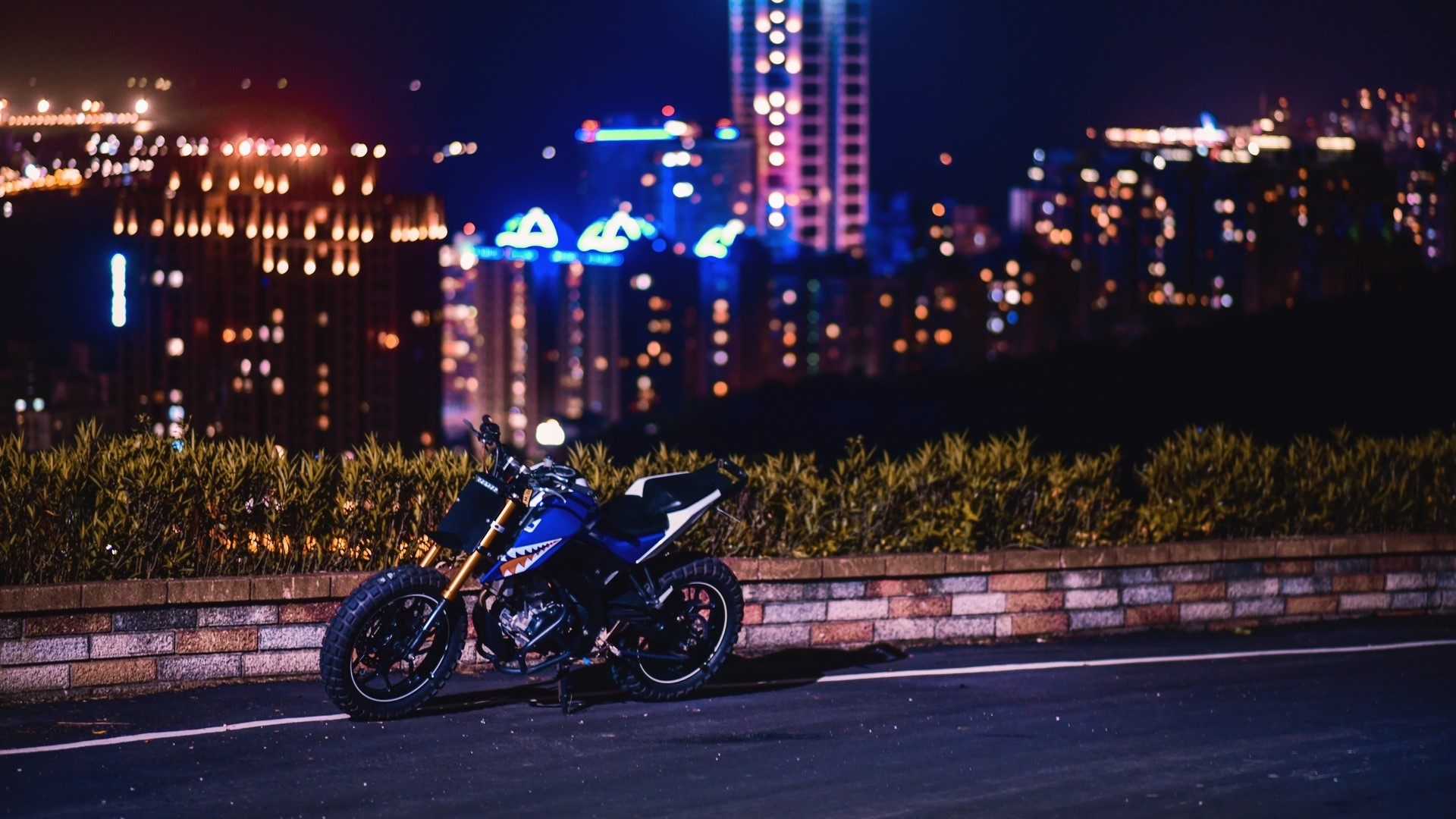 Blue motorcycle parked at night with city lights HD Wallpaper