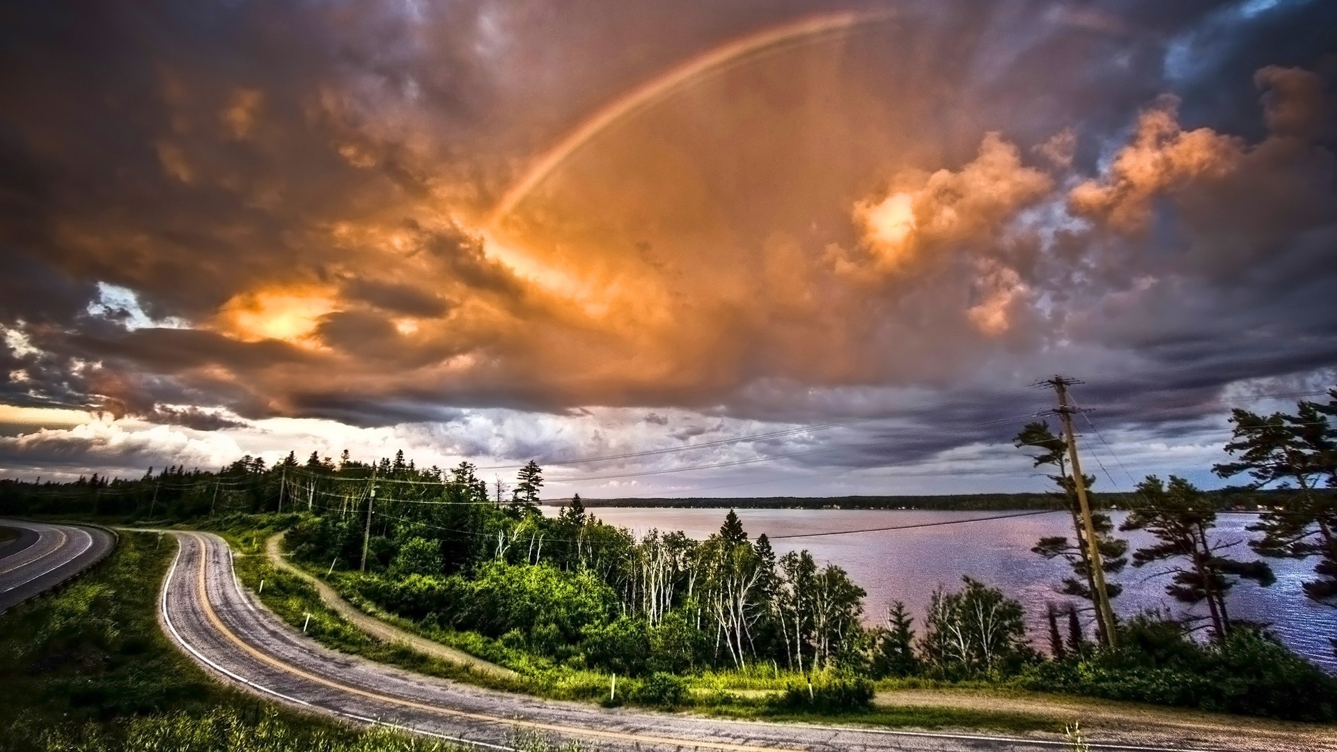 Rainbow over a winding road and a lake HD Wallpaper