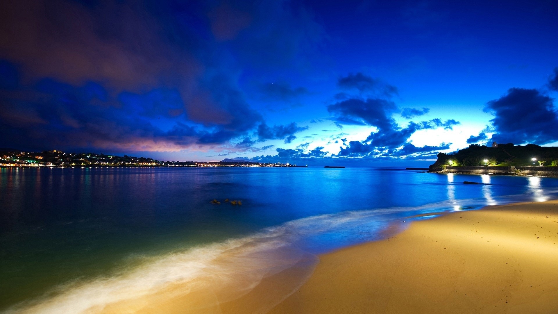 Beach at dusk with city lights reflecting on the water HD Wallpaper