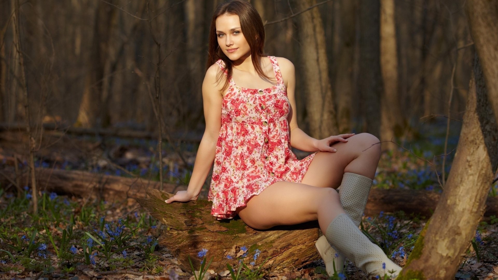 Woman in floral dress sitting on a log in a forest HD Wallpaper