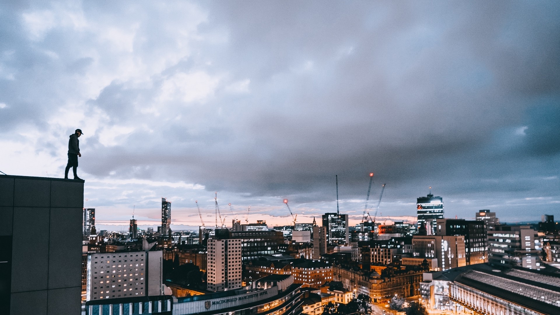 Person standing on a rooftop overlooking a city at dusk HD Wallpaper