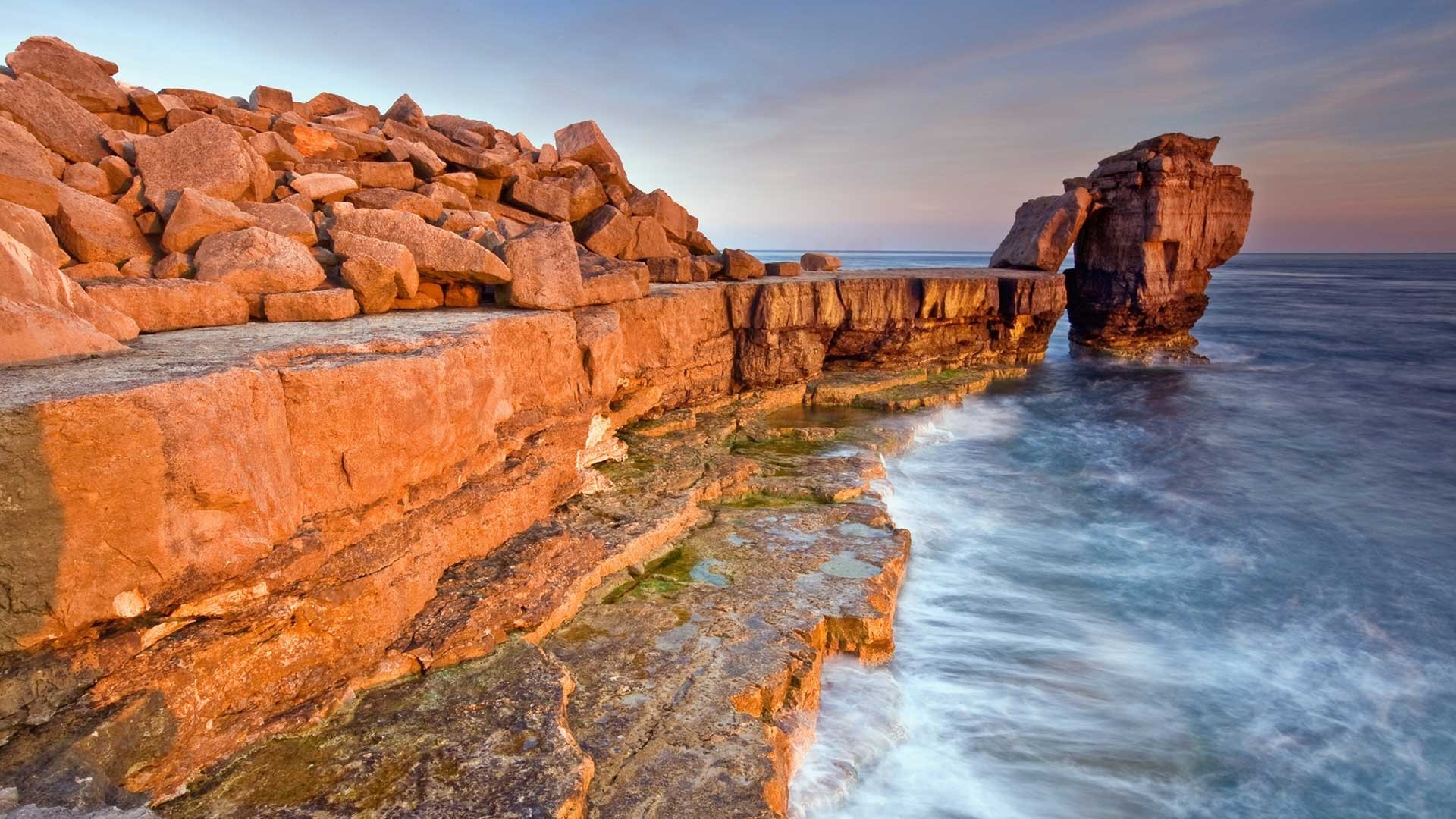 Orange rock formations on a coastline with waves HD Wallpaper