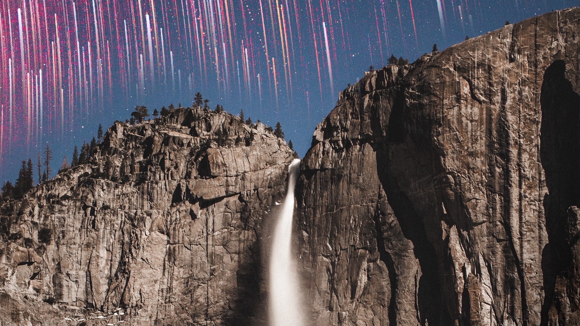 Waterfall cascading down rocky cliffs under a starry sky with light streaks HD Wallpaper