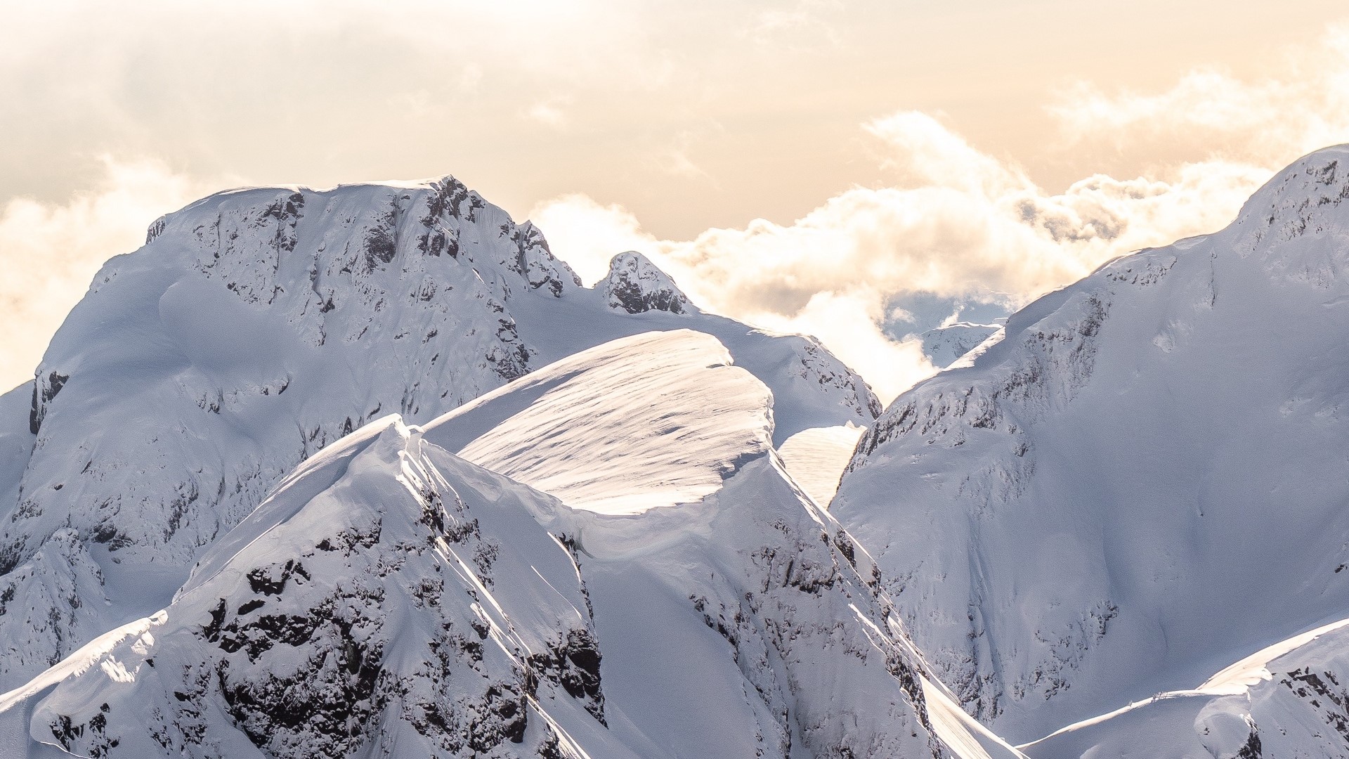 Snow-covered mountain range under a cloudy sky HD Wallpaper