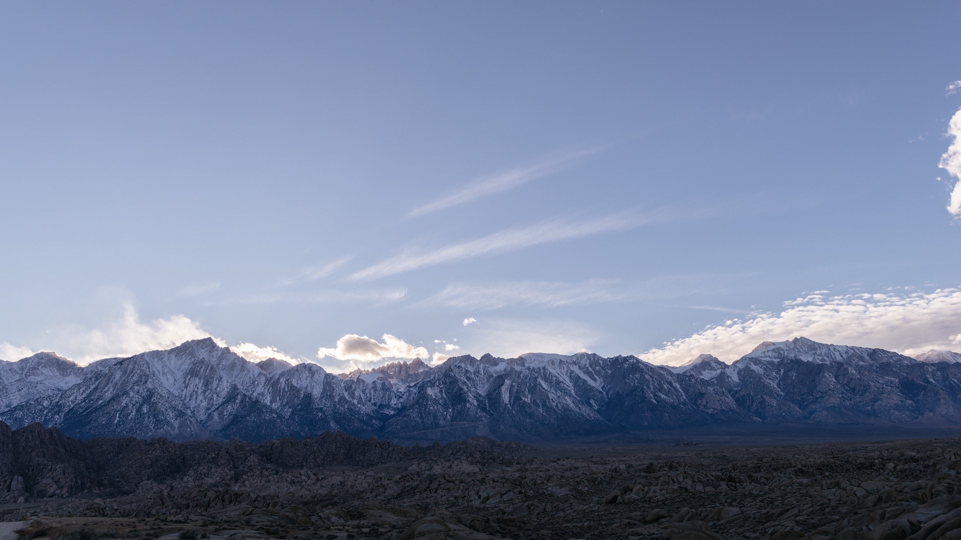 Snow-capped mountains under a pale blue sky HD Wallpaper