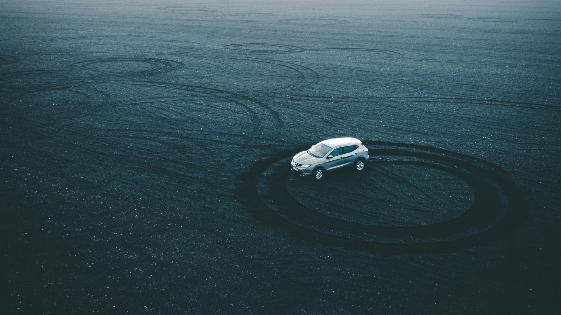 Nissan car on black sand with tire tracks HD Wallpaper