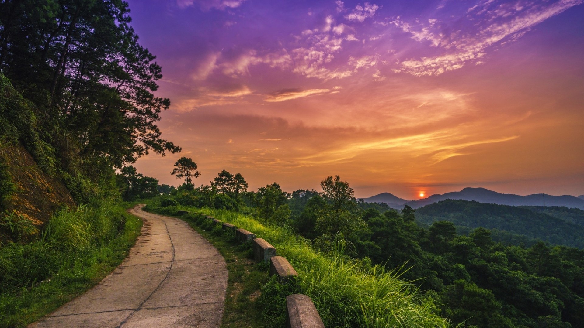 Mountain road at sunset with purple and orange sky HD Wallpaper