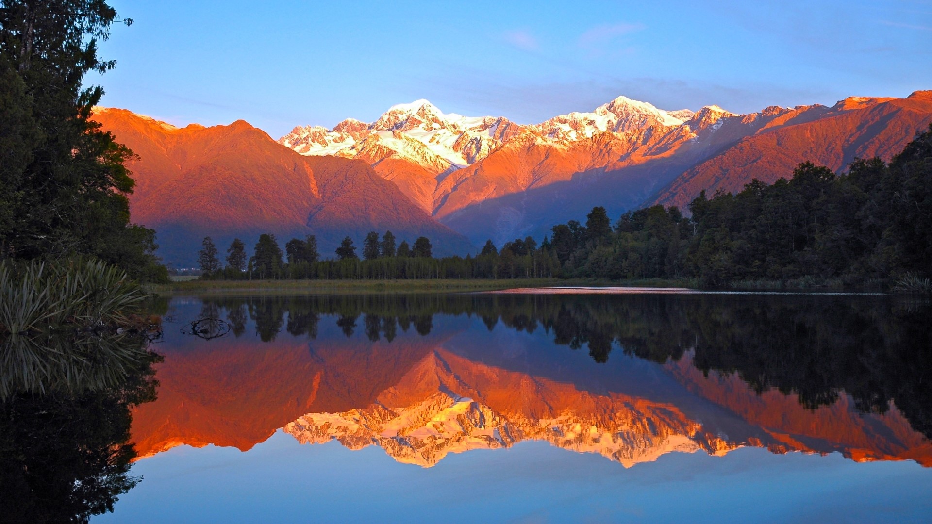 Snow-capped mountains reflected in a lake at sunset HD Wallpaper