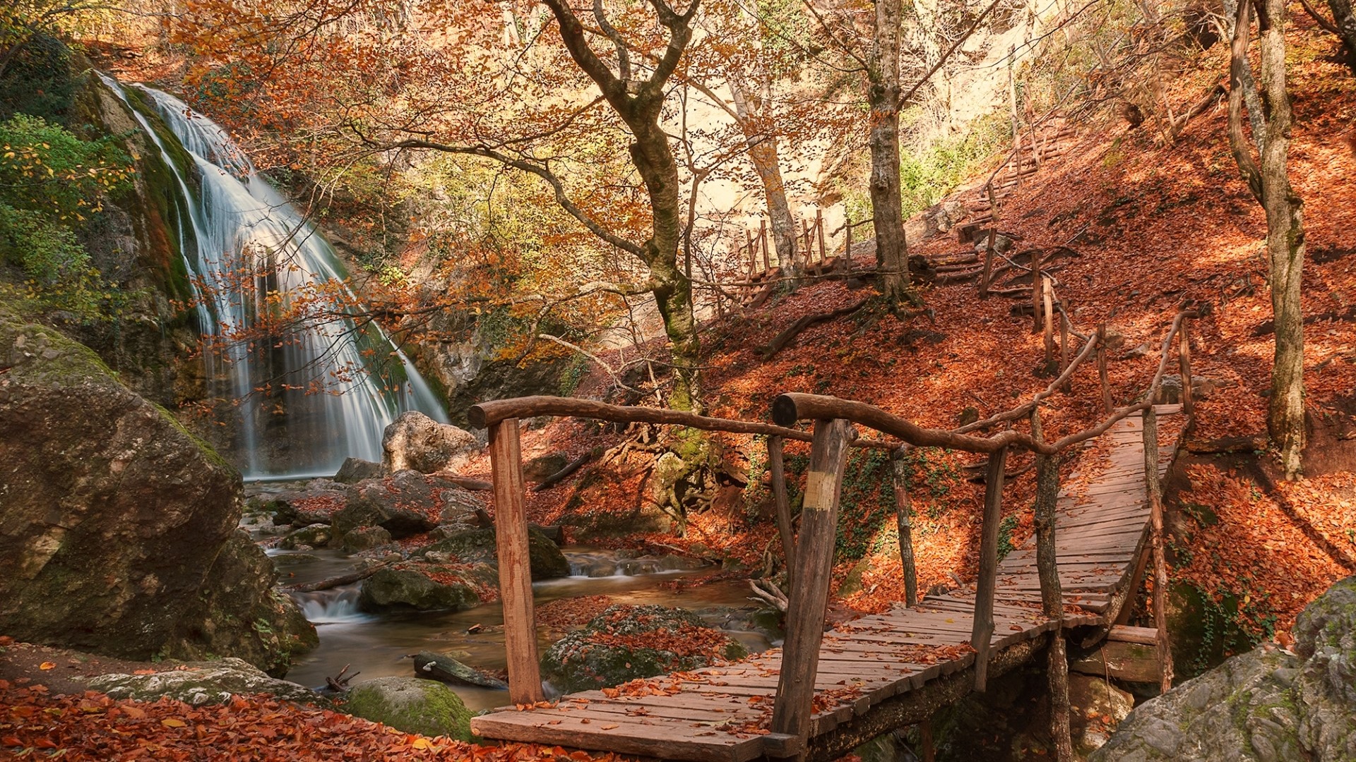 Wooden bridge over stream near waterfall in autumn forest HD Wallpaper