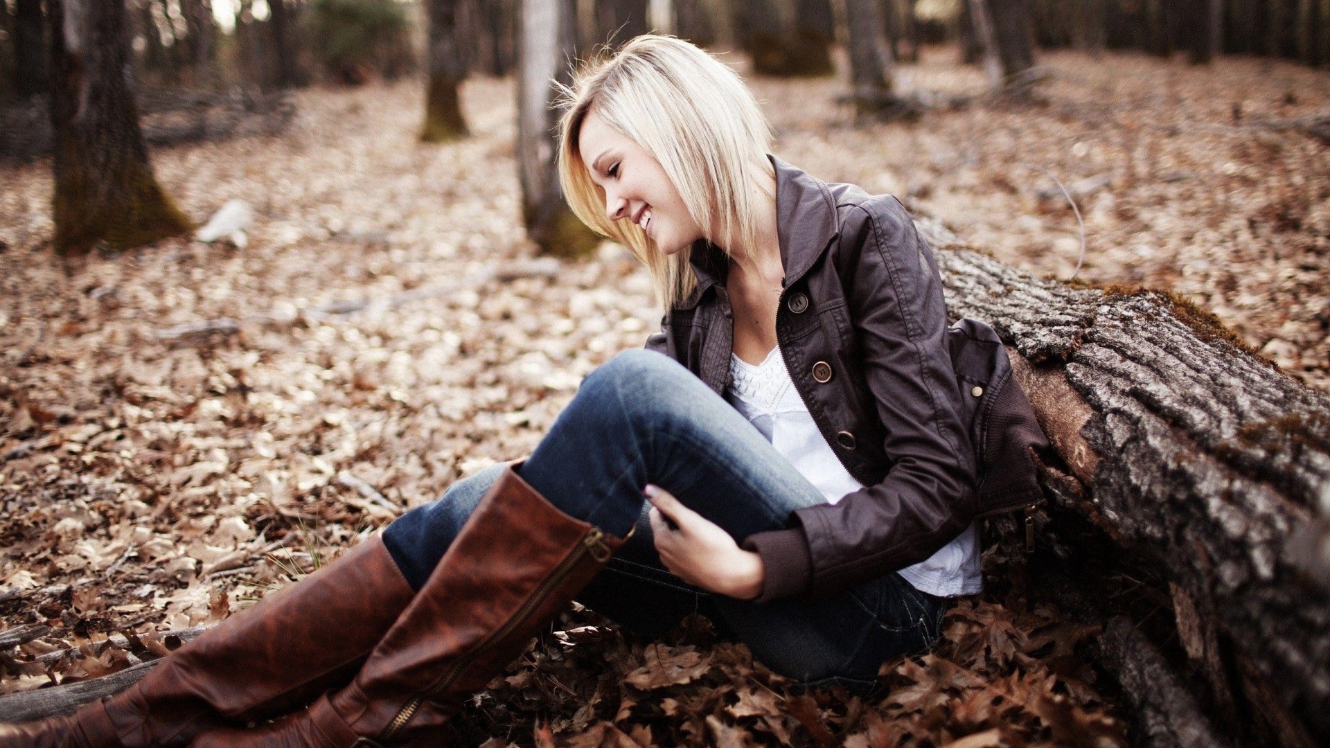 Blonde woman sitting in a forest with fallen leaves HD Wallpaper