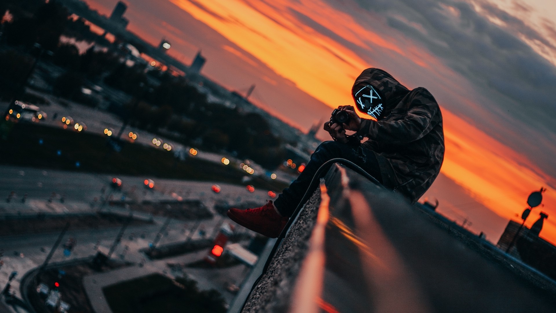 Person in mask with camera on rooftop at sunset HD Wallpaper