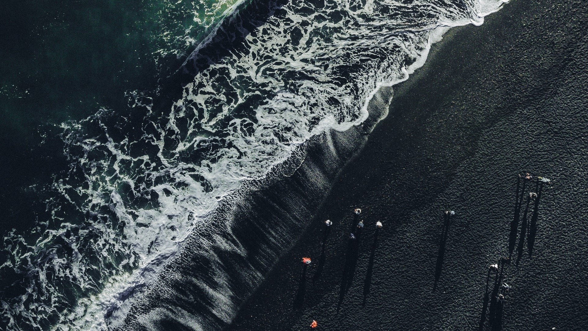 Aerial view of a black sand beach with waves and people HD Wallpaper