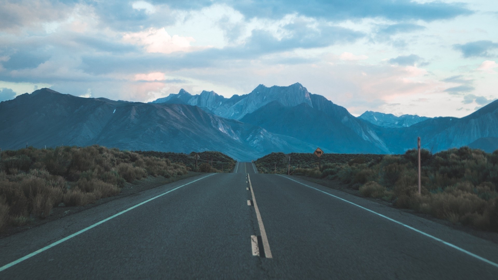 Road leading to mountains under cloudy sky HD Wallpaper