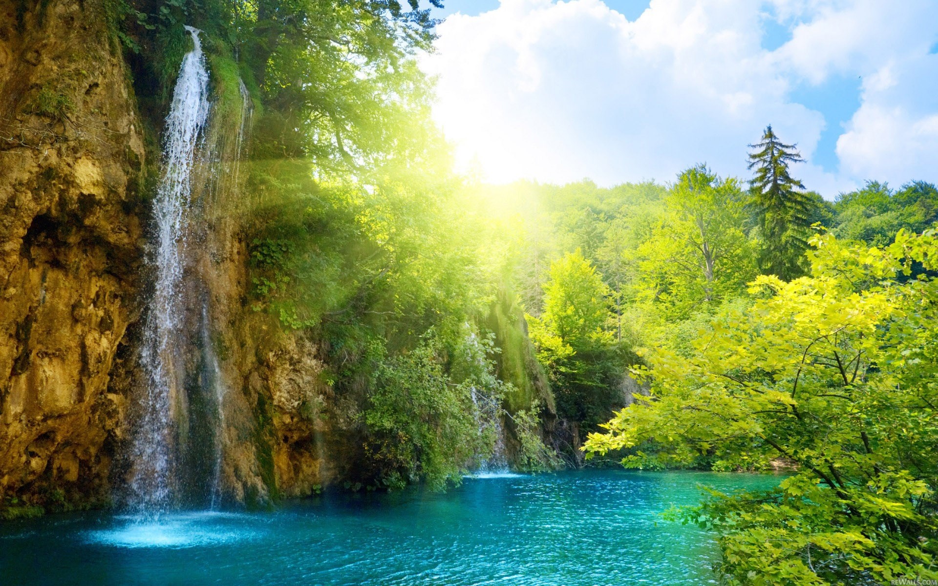 Waterfall cascading into a turquoise lake surrounded by lush green forest HD Wallpaper