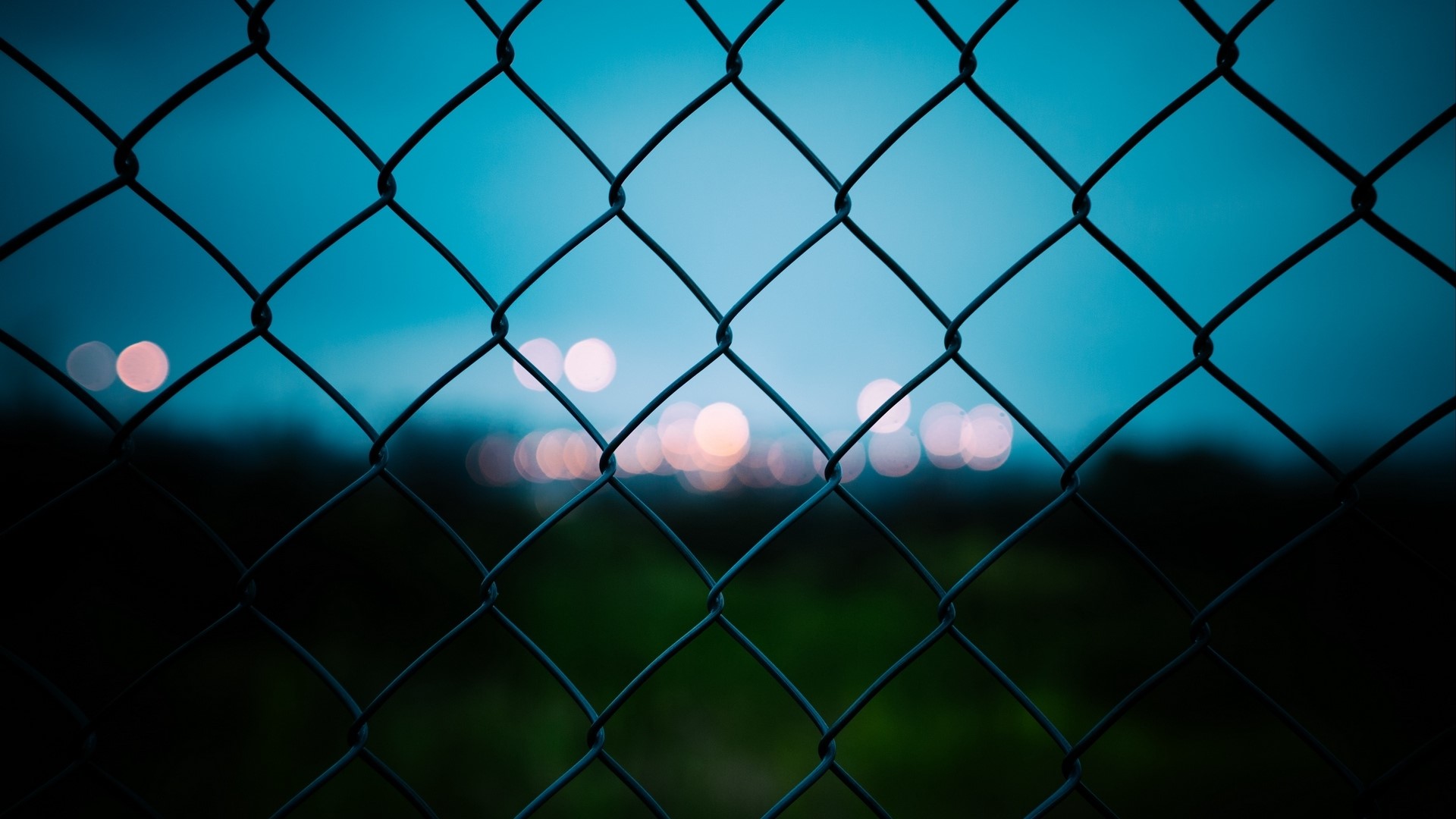 Chain-link fence against a twilight sky with bokeh lights HD Wallpaper