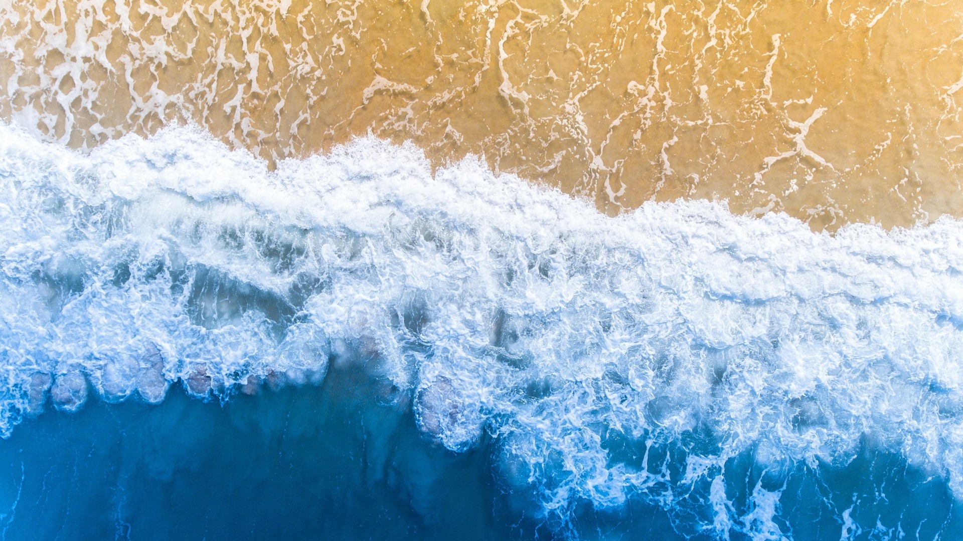 Aerial view of ocean waves crashing on a sandy beach HD Wallpaper