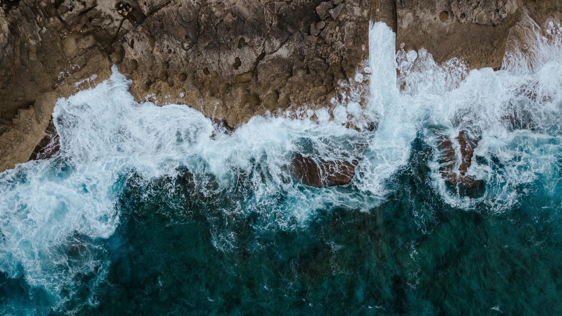 Aerial view of waves crashing on rocky shore HD Wallpaper