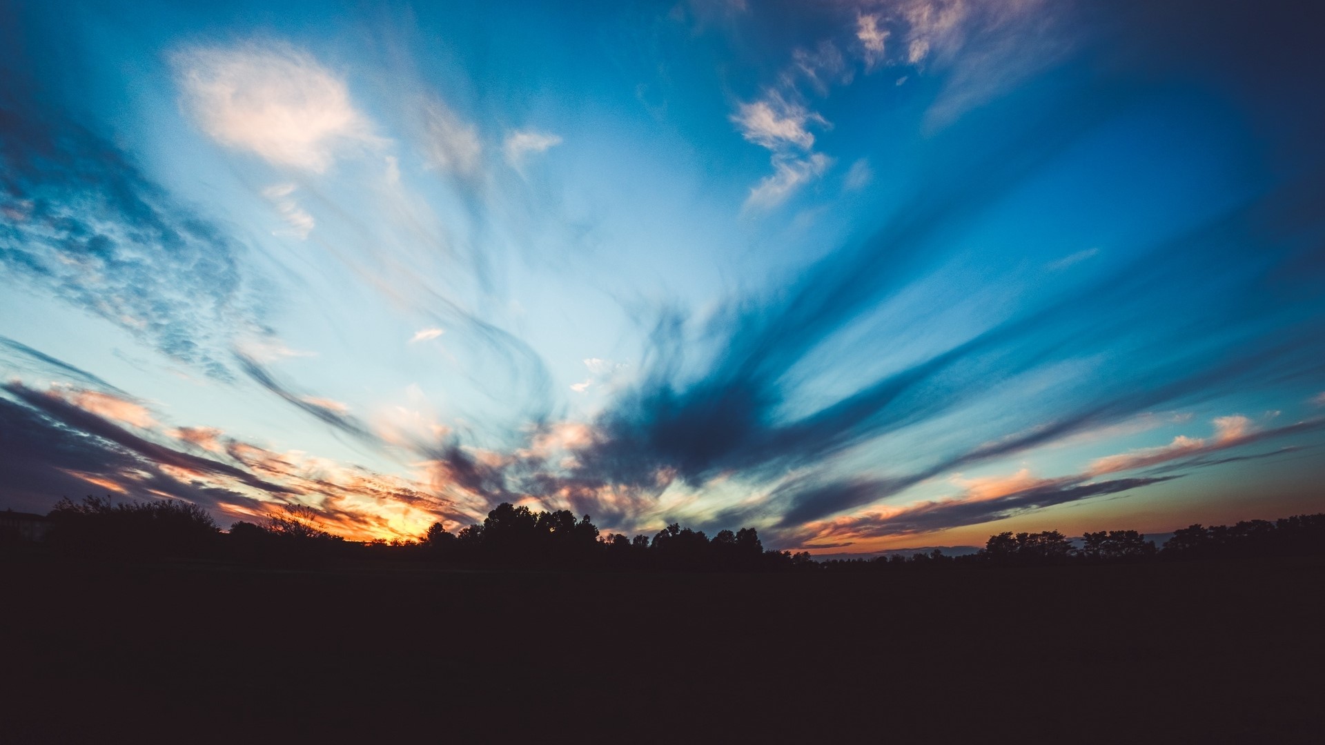 Dramatic sunset sky over silhouetted trees HD Wallpaper