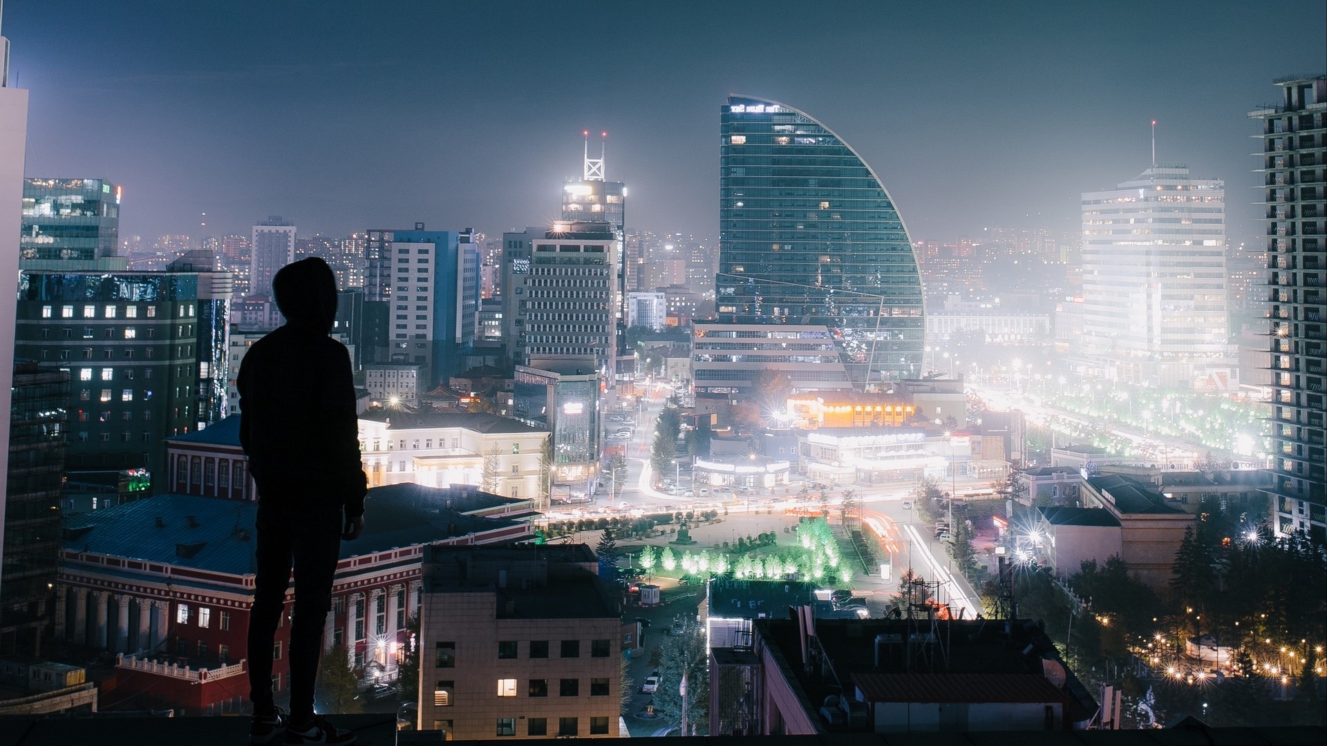 Silhouette of a person on a rooftop overlooking a city at night HD Wallpaper
