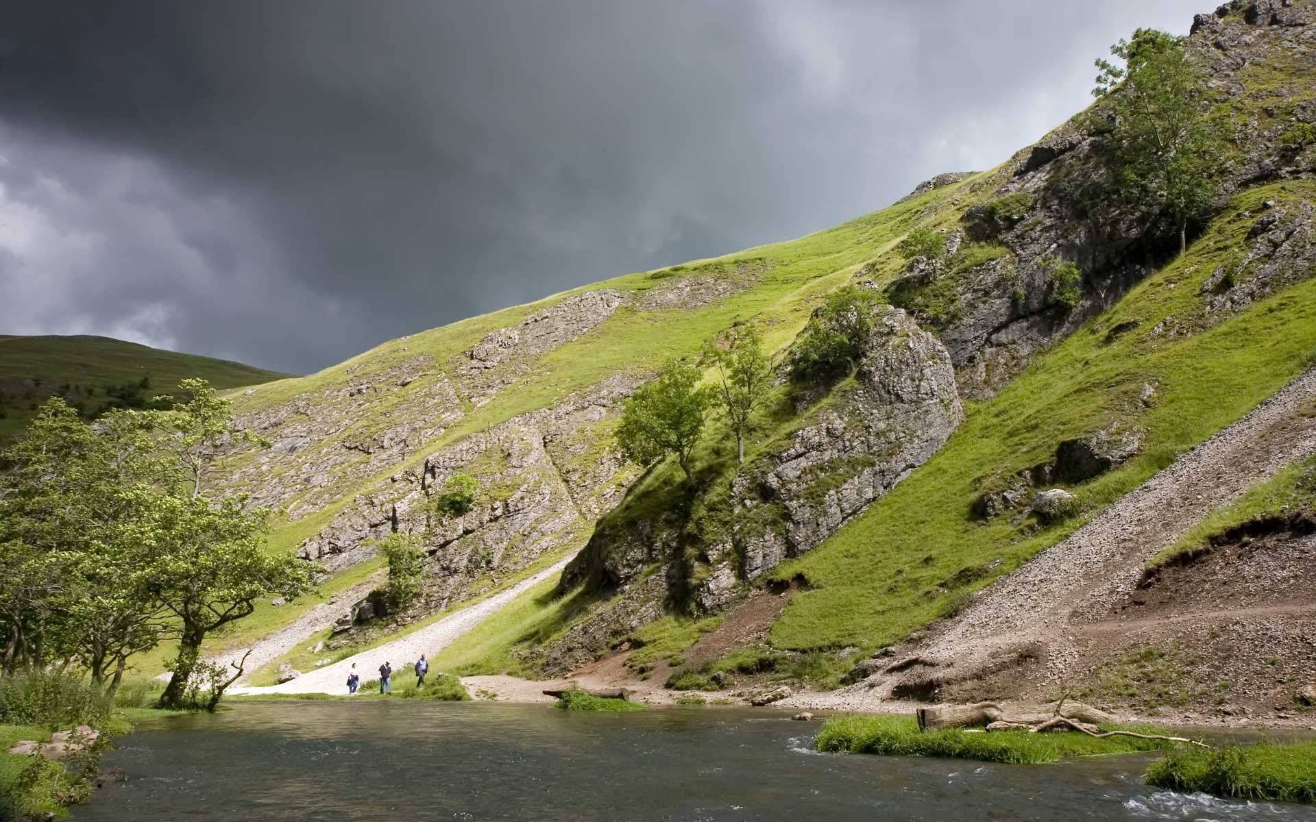People walking by a river in a rocky valley HD Wallpaper