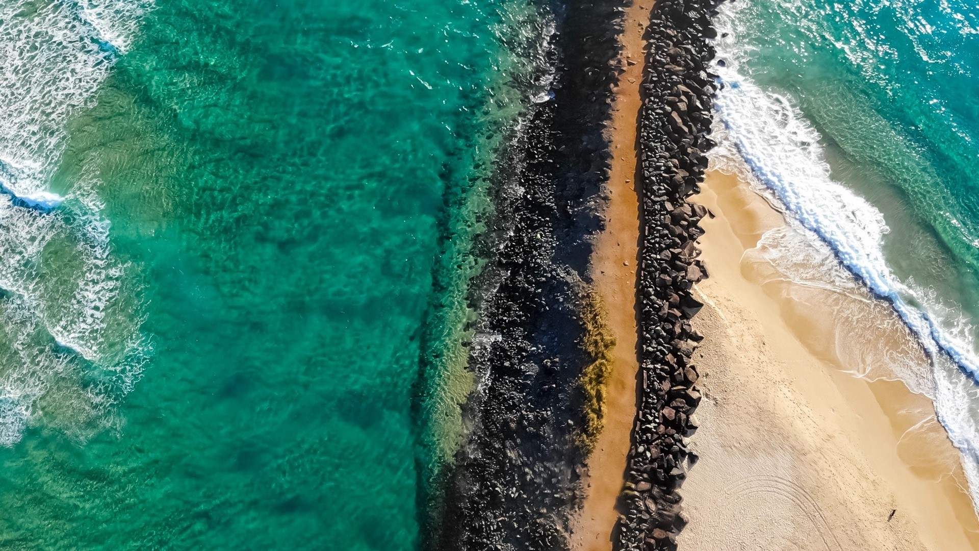 Aerial view of a rocky breakwater and ocean waves HD Wallpaper