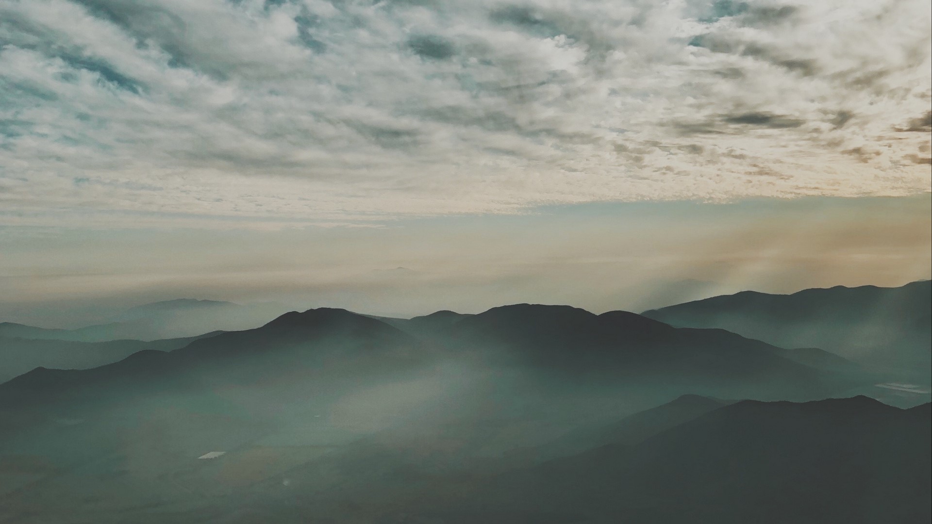 Mountain range shrouded in fog with sunbeams HD Wallpaper