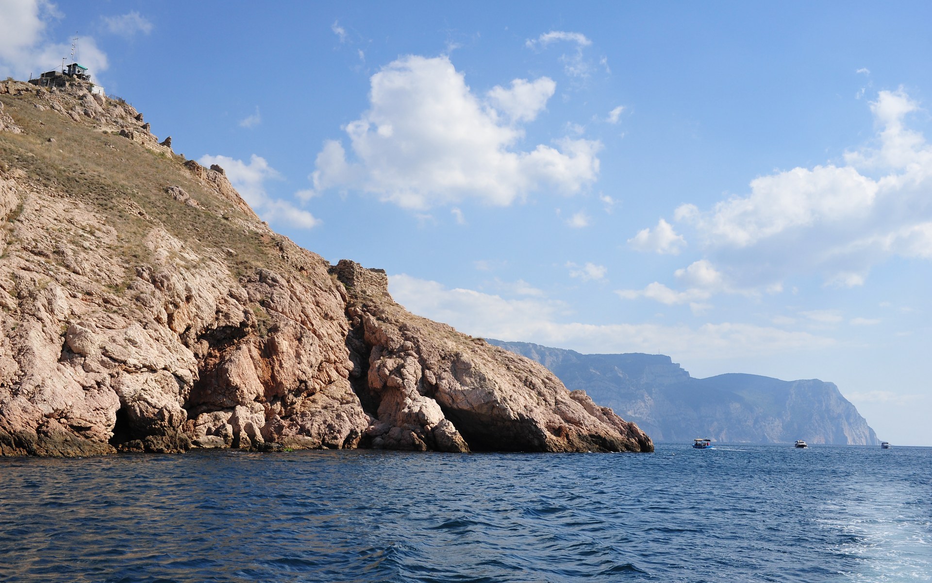 Rocky coastline with caves and boats on the sea HD Wallpaper
