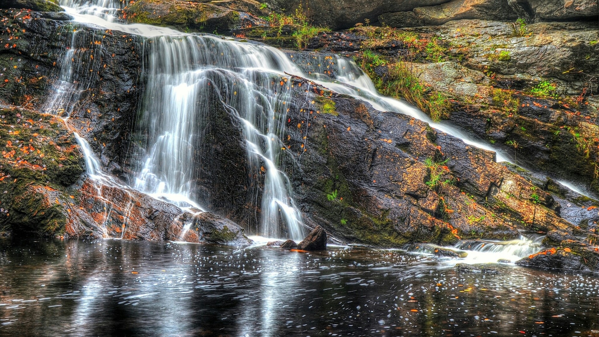 Waterfall cascading over dark rocks into a pool HD Wallpaper