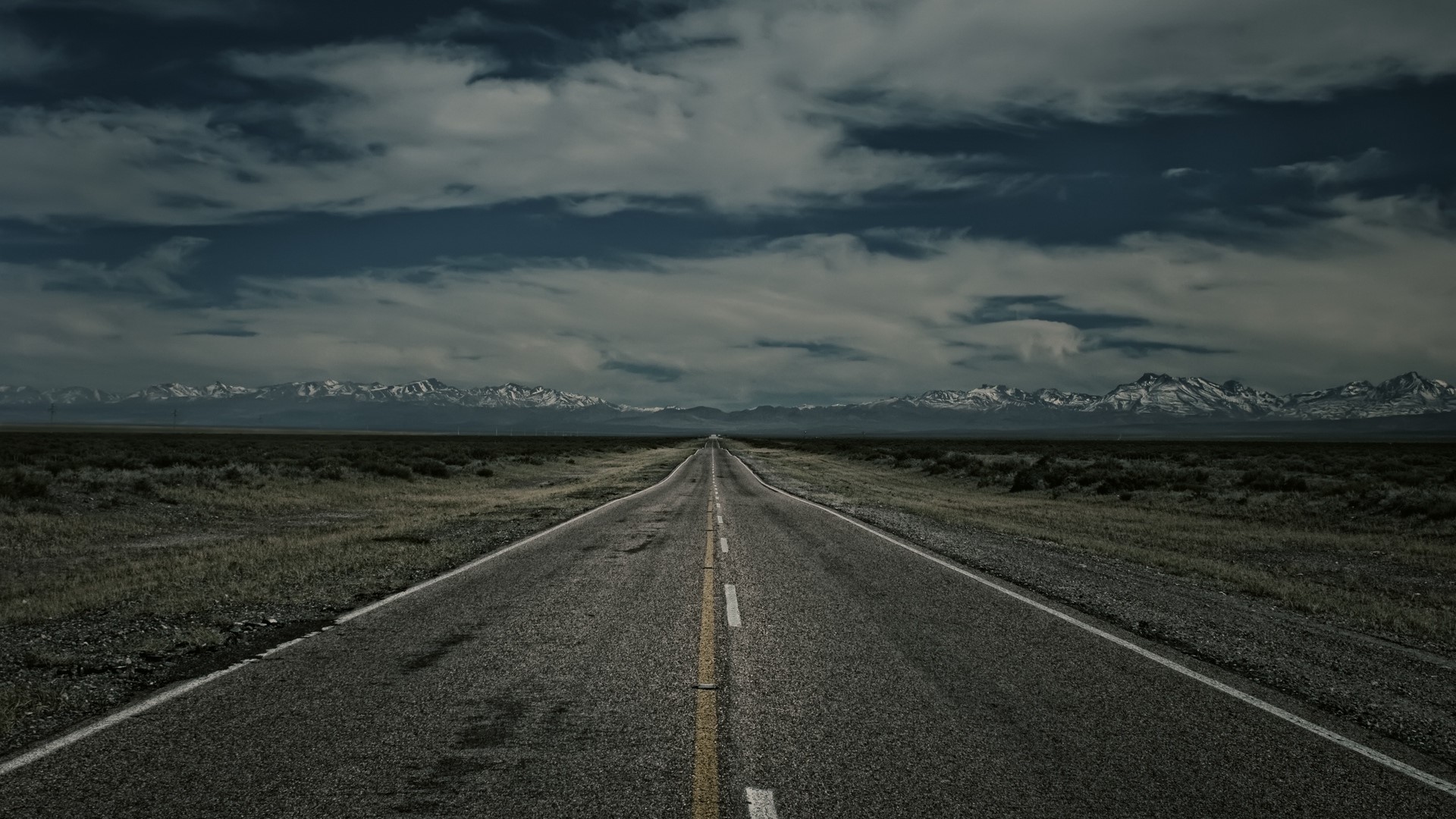 Road leading to snow-capped mountains under cloudy sky HD Wallpaper