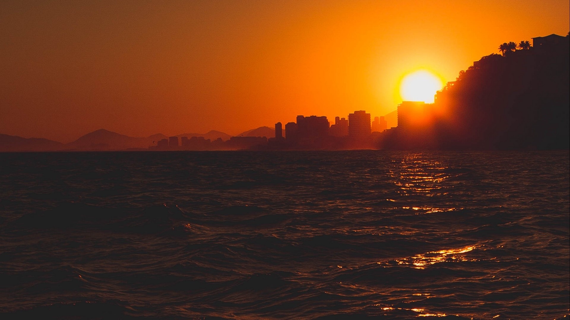 Sunset over ocean with city skyline HD Wallpaper
