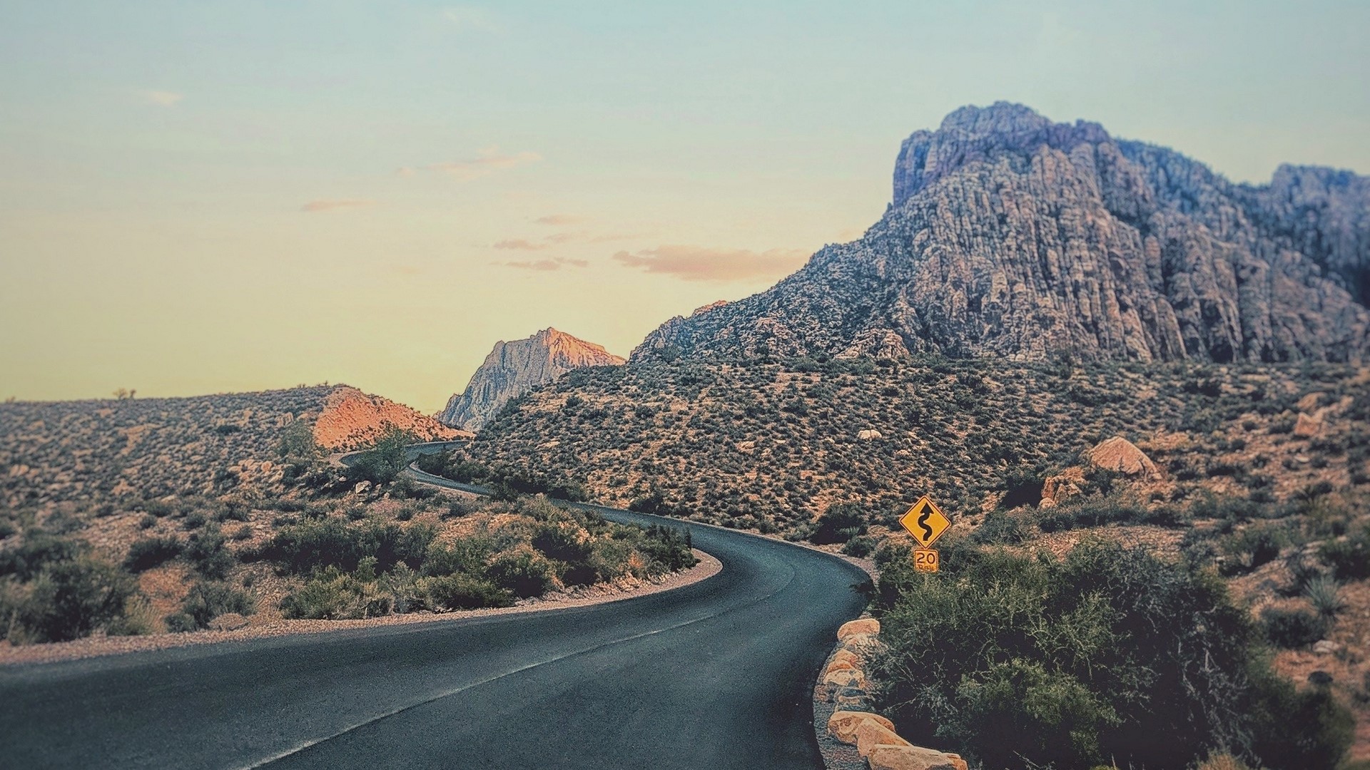 Scenic mountain road with a curve and a warning sign HD Wallpaper